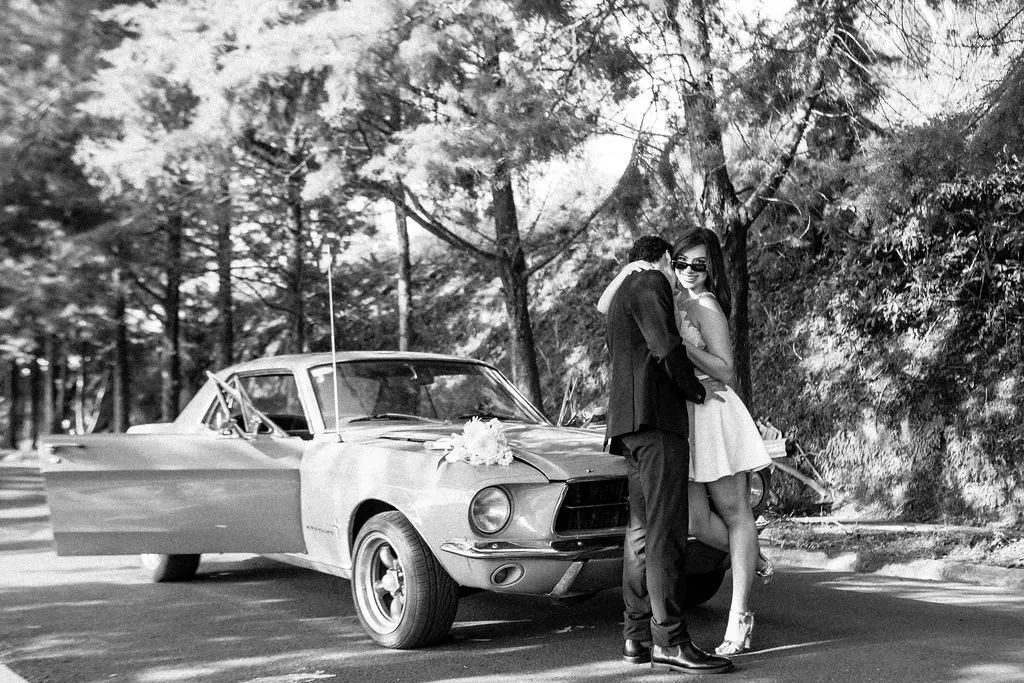En blanco y negro, un beso junto al Mustang decorado con flores